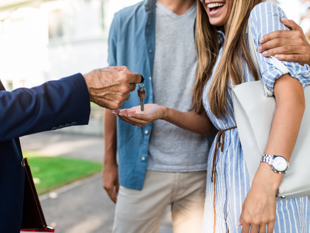 a woman extends her hand to a realtor beside her partner as they hand her keys to a new home they purchased using mortgage financial readiness tips